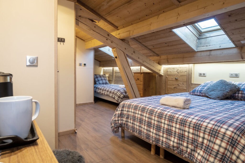 Interior of Bedroom 2 in Chalet Aventure, featuring a double bed, single bed, TV, ensuite shower room, and coffee-making facilities.