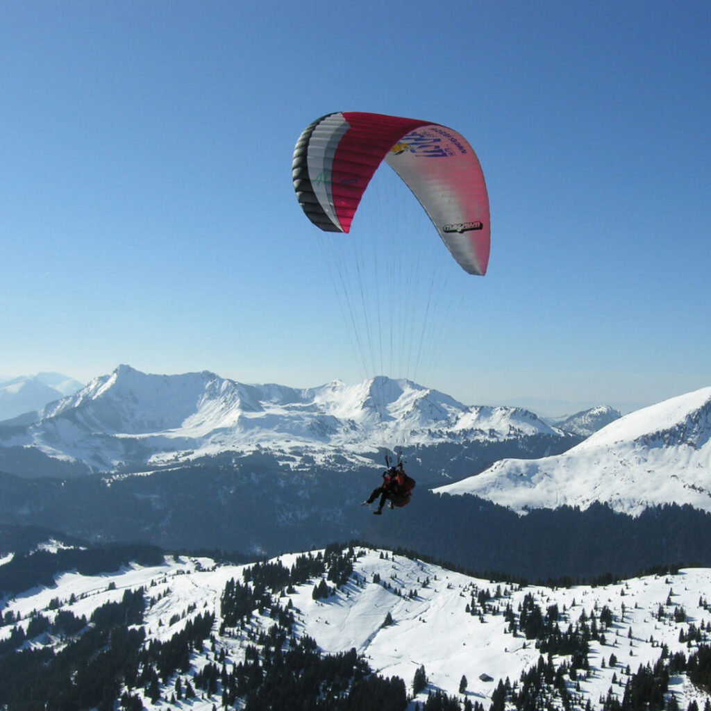 Paraglider soaring over the snow-covered mountains above Les Gets in winter.