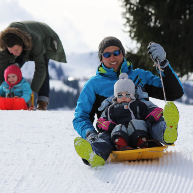 Father and child enjoying a fun sledge ride down a toboggan piste in Les Gets.